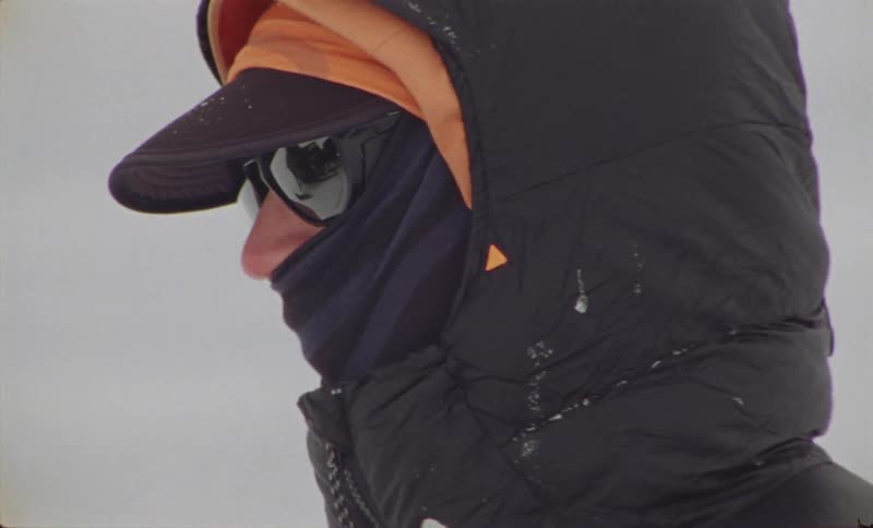 A person so bundled in winter clothing that their nose is the only body part visible looks around while standing outdoors in the snow