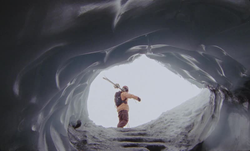 A person standing in front of an ice tunnel and holding ski equipment and then he starts walking