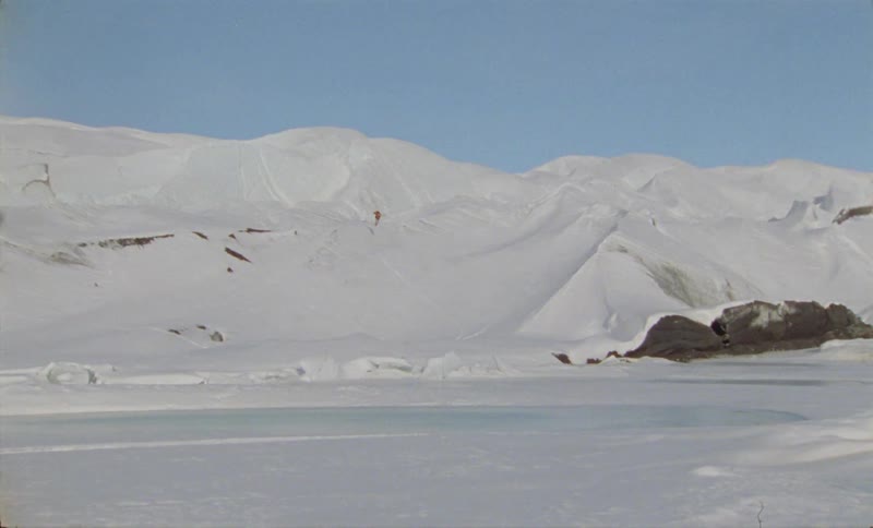 A person skiing with expansive view of snowy mountains and icy terrain under a clear blue sky