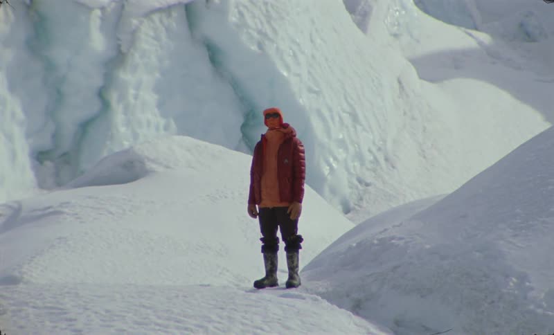 A person bundled up for the cold stands on a snow covered ridge near mountains