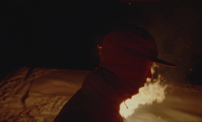 Man walks around a fire in the snow at night