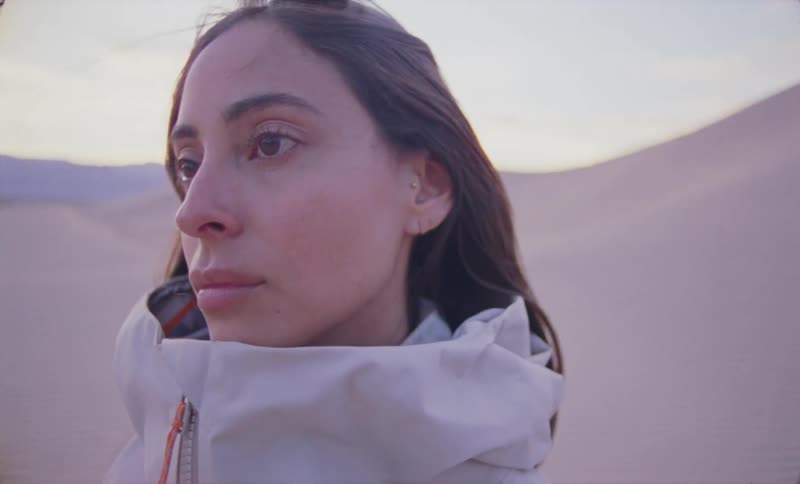 The face of a young woman who is wearing a warm outfit that goes up to her neck and she is looking to her left side where there is a desert