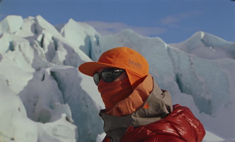 Person in winter cap and jacket stands in ice mountains environment during daytime