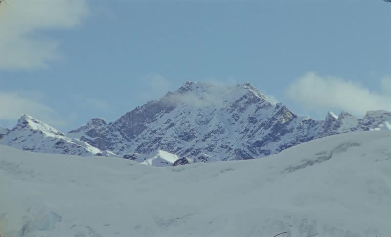 Peak of snowcapped mountains under wispy clouds in a blue sky