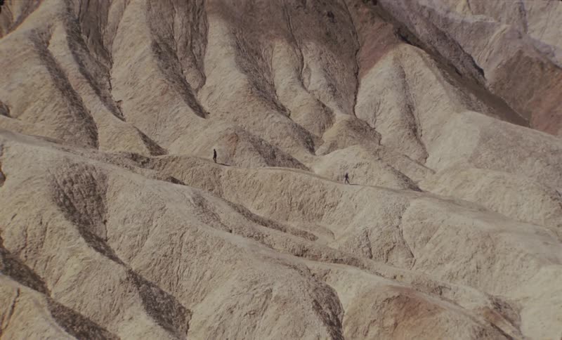 Two people walking through desert mountains in broad daylight