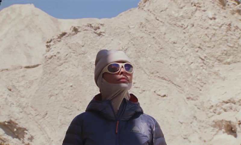 Woman wearing fashionable cold weather attire stands next to a stone cliff on a sunny day
