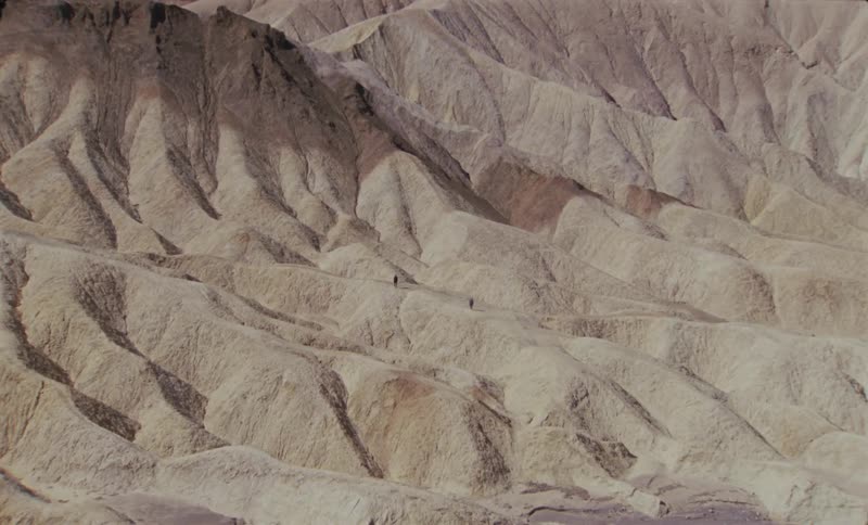 People stand on the samefoothill in arid terrain near the mountains