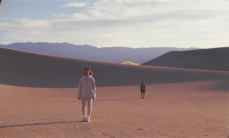 Two people are standing in the desert on a windy day