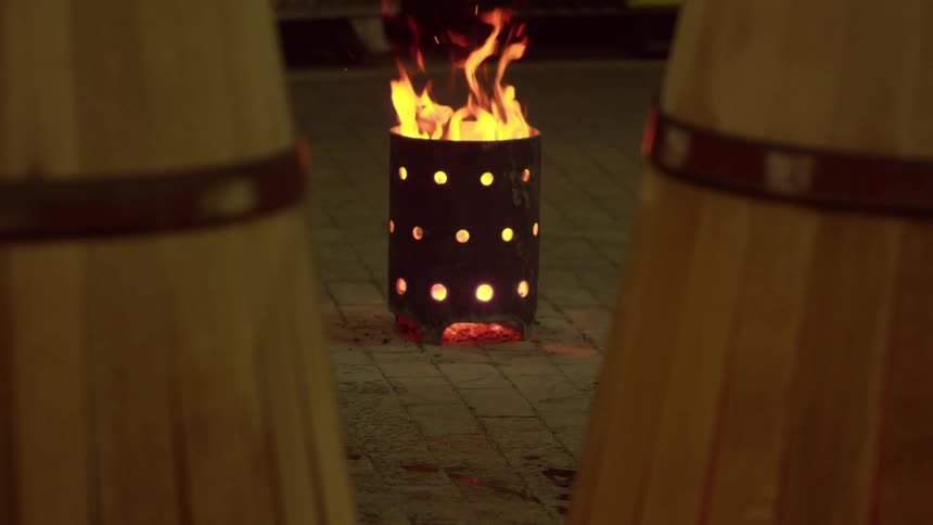 A person moves a barrel past a pot with a fire burning in it