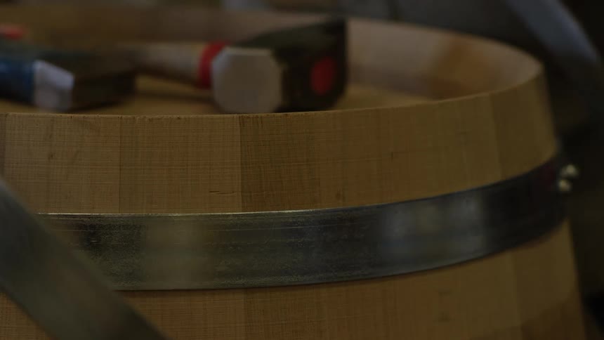 A closeup of a wooden barrel with a hammer resting on its rim suggesting craftwork or construction