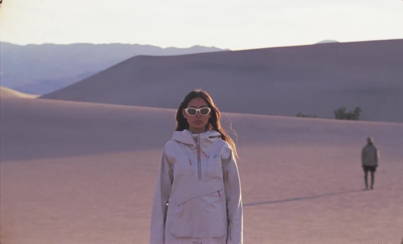Two people standing in an empty desert and the woman who is closest to you is wearing white clothes and sunglasses