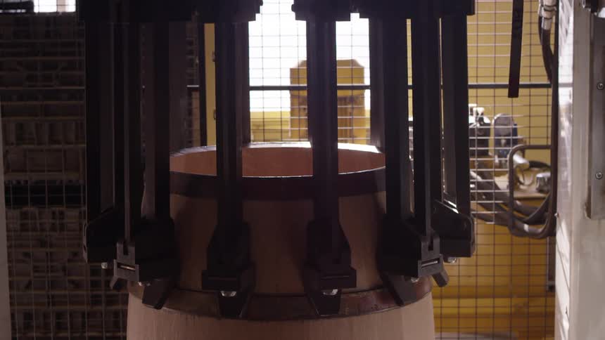 A machine with several circular hooks passing over the outer surface of a wooden barrel and then rising up