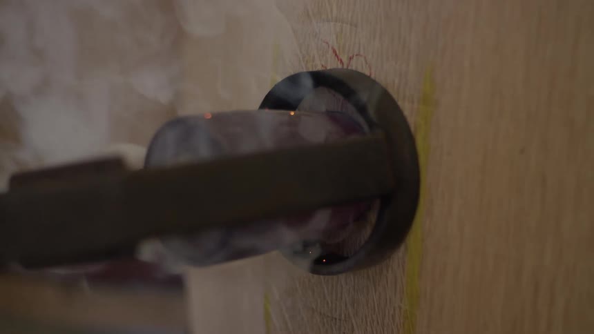 A tool emitting smoke while pressing against a wooden surface creating a hole