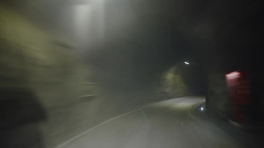 A curve inside a tunnel that has an asphalt street and low lighting on the walls