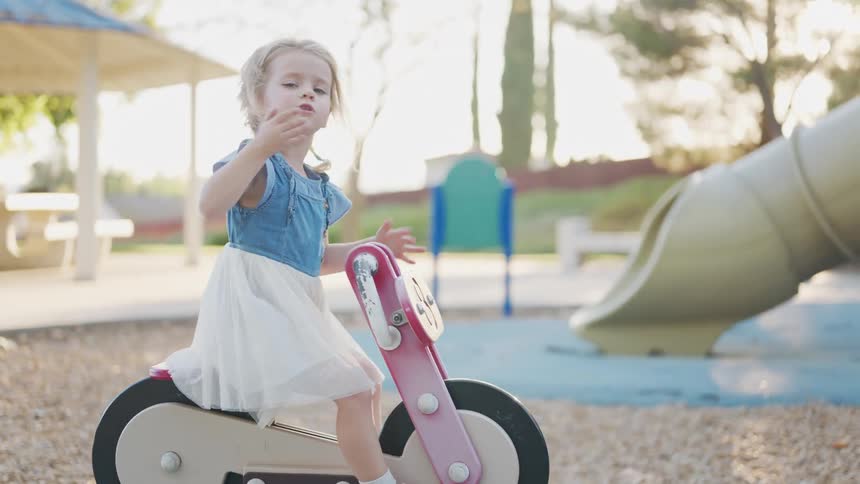 A child is riding a stationary playground motorcycle toy in an outdoor park area