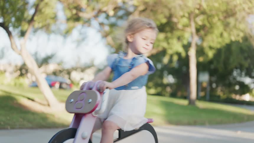 A little blonde girl is playing on top of a bicycle where she is moving back and forth
