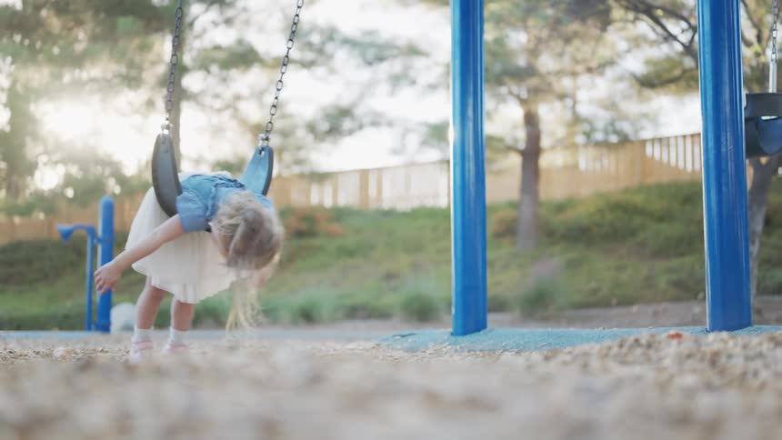 Little blonde girl playing on a swing in a playground