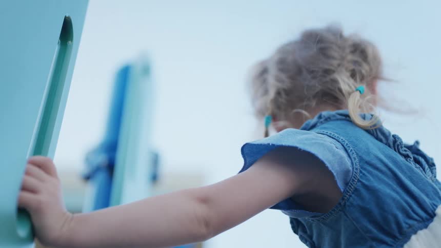 Little blonde girl climbing on a toy in a playground