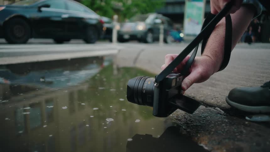 Photographer holds a camera near a puddle to take a picture of a car and its reflection