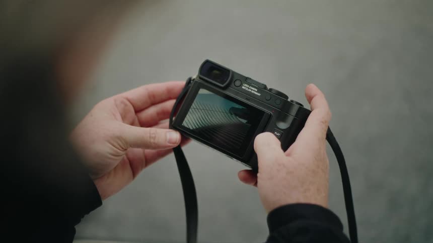 A man looks at his camera and pushes a button to flip between different frames of a photo