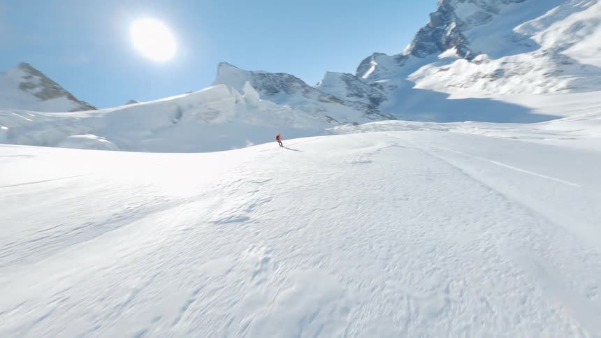 A Lone Skier Skiing Over a Glacier in the Backcountry Under a Clear Blue Sky