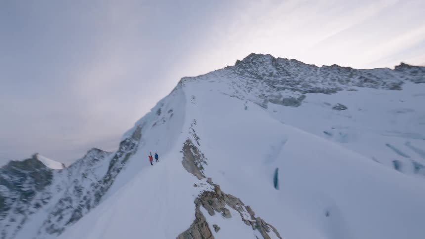 Aerial view of two mountaineers trekking along a snowy ridge with towering peaks in the background