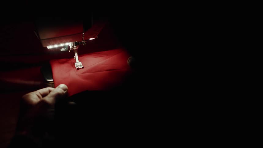 Hand holding red fabric being sewn on a machine in a dark room