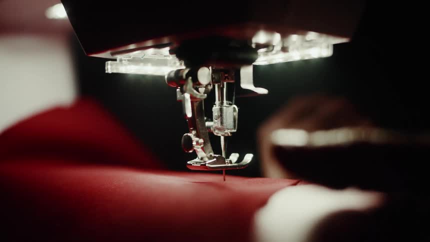 Close up of a hand handling red fabric on a sewing machine