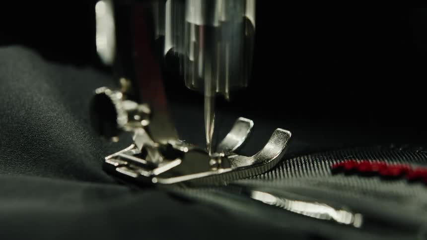 A detailed view of a sewing machine needle crafting stitches on dark fabric