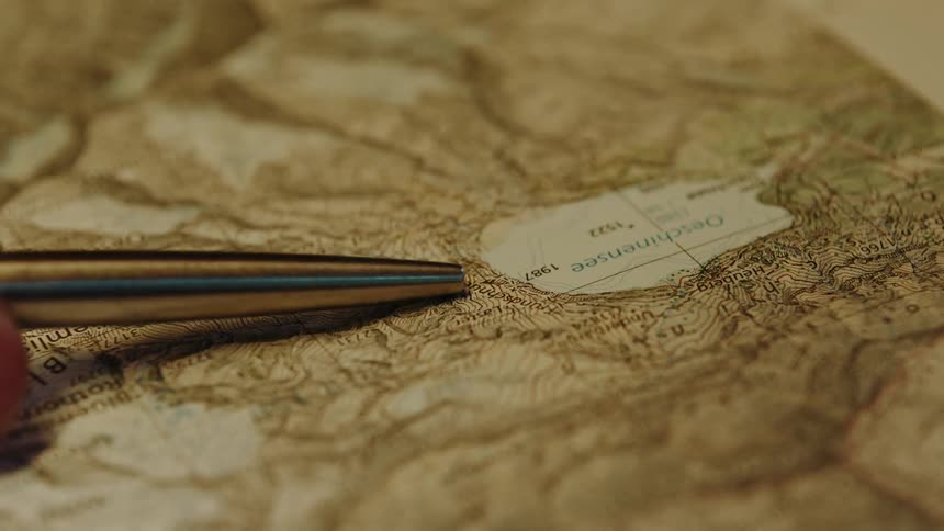 A gold pen hovers over a weathered map its tip poised to mark a destination
