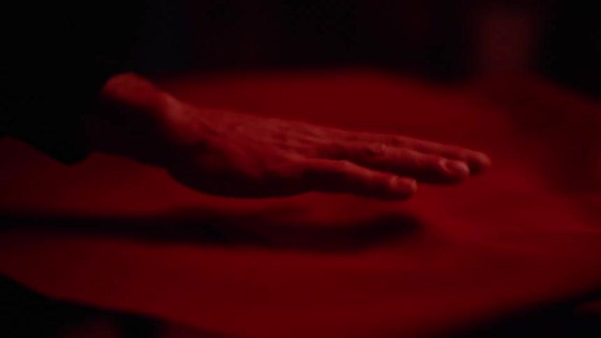 A persons hand passing its palm over the surface of a red fabric