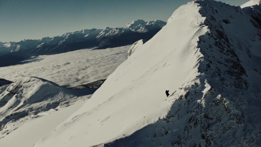 A lone figure climbing a snowy mountain ridge