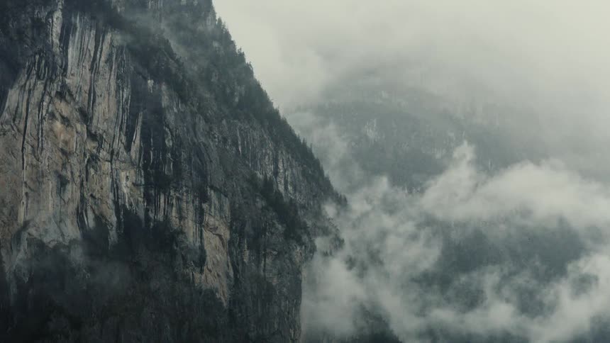 Low lying clouds obscure conifer covered mountains near a cliff on a cloudy day