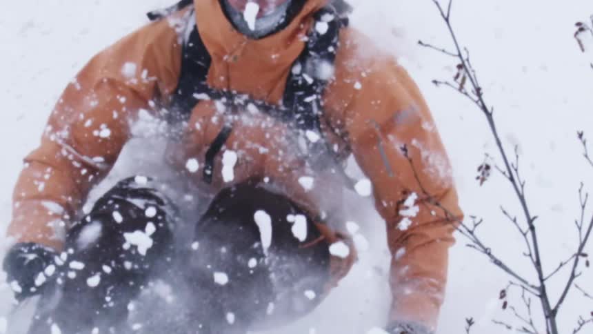 Skier sends snow into the air while skiing down a snow covered slope between leafless trees