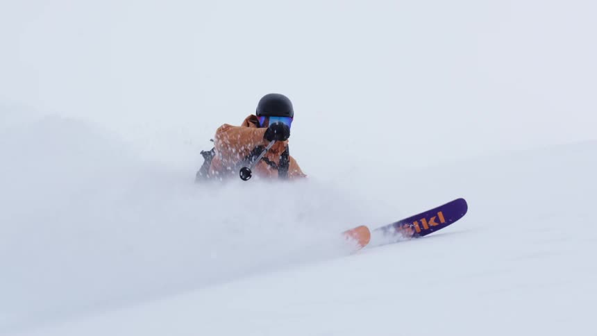 A person skiing and then skidding with their ski kicking up a lot of snow