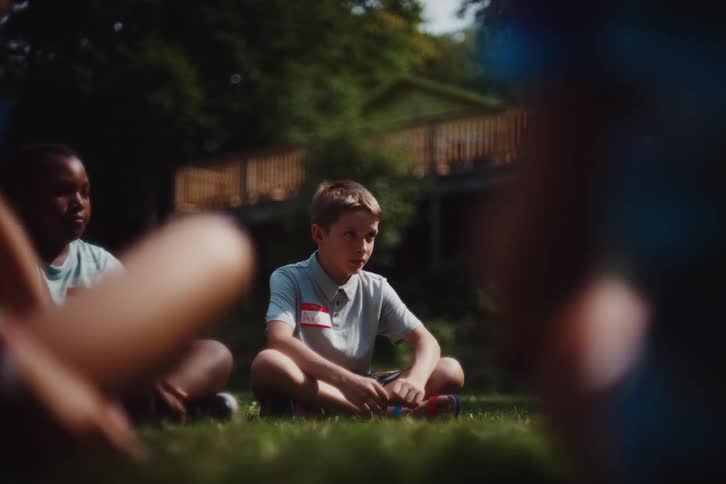 Kids sitting on the ground yell during a group activity before standing