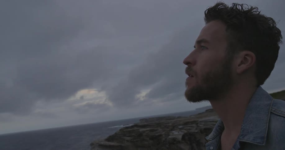 Person atop a rocky hill looking out of the water