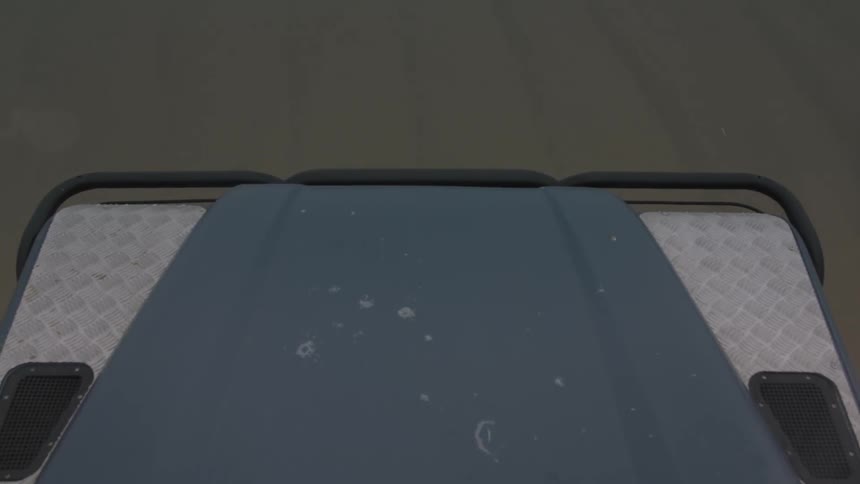 A car is driving and we see only the hood as it is passing over a dirt road