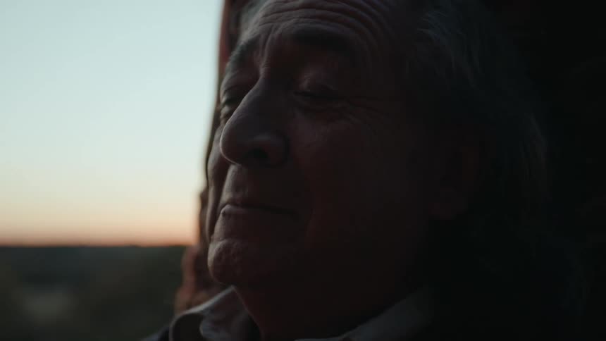 Elderly man sits outdoors while red tints the horizon