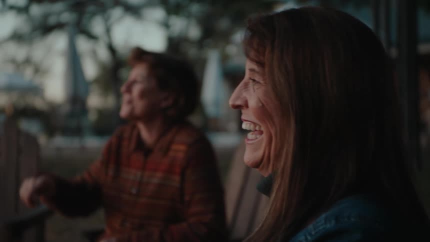 Two women sitting on wooden chairs laughing out loud in a backyard in the late afternoon