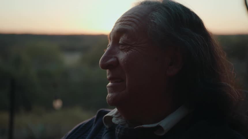 An elderly man speaks while outdoors in nature