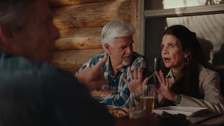 People sitting outside at a table with food and beers and laugh while having a conversation