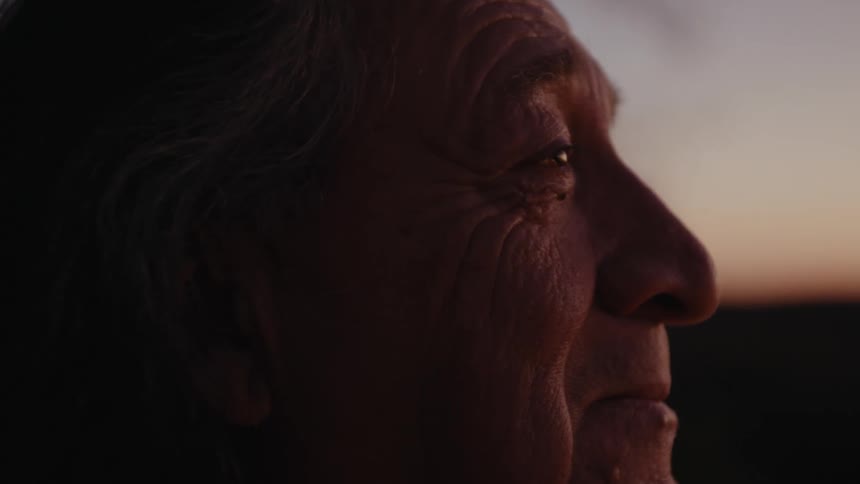 An elderly native american man outdoors staring into the distance while smiling and thinking