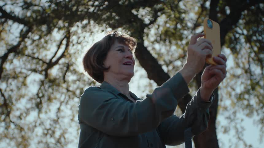 A woman takes a selfie outdoors with a tree canopy visible in the background