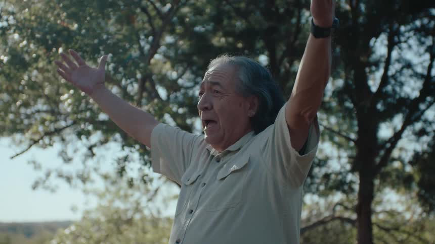 Elderly man happily cheering with his family around in a garden with trees