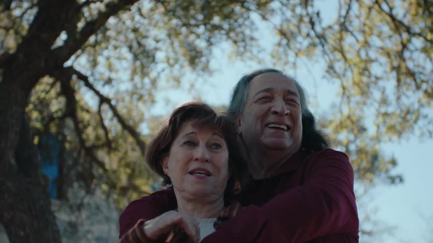 A couple embrace outside their home underneath a tall tree in the yard