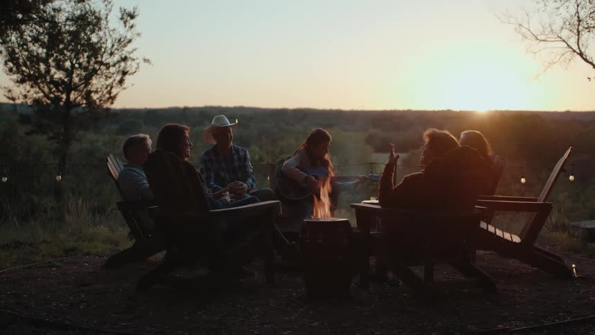 A serene gathering around a campfire at sunset with music and laughter filling the air