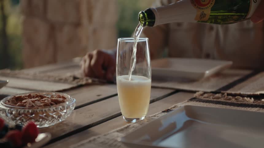 A man sits at a dining table on a patio while another person pours wine into a glass