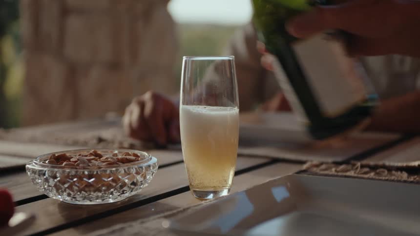 A group of people pouring and passing around a sparkling drink at a table containing snacks outdoors on a sunny day