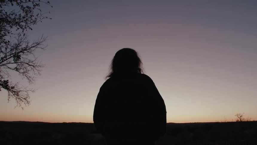 Older man stands looking towards the red tinted horizon